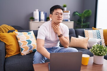 Sticker - Young asian man using laptop at home sitting on the sofa touching painful neck, sore throat for flu, clod and infection