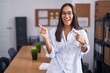 © Krakenimages.com - Young hispanic woman at the office smiling and looking at the camera pointing with two hands and fingers to the side.