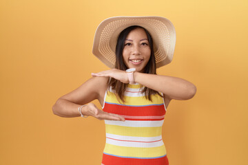 Wall Mural - Middle age chinese woman wearing summer hat over yellow background gesturing with hands showing big and large size sign, measure symbol. smiling looking at the camera. measuring concept.