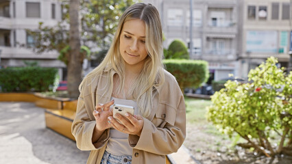 Sticker - Beautiful blonde, a young woman with a cool, casual lifestyle, standing seriously in a sunny park, fully concentrated on her smartphone while texting online