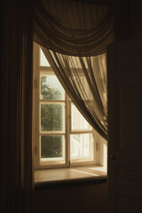  A picture of a window with the curtains ajar. Sunlight penetrates through the curtained window. How the windows were decorated at the end of the XIX century.
