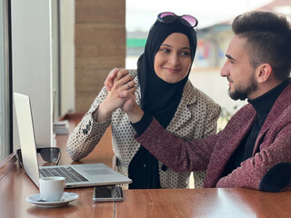 Wall Mural - A young happy Muslim couple together working on a laptop and using a mobile phone at cafe restaurant or office.