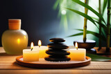 Fototapeta Sypialnia - Stacked round black stones, sea salt, massage oil and burning candles with warm light on a wooden tray on a table with bamboo leaves in a spa salon. Beauty therapy, aromatherapy, relax, zen concept.