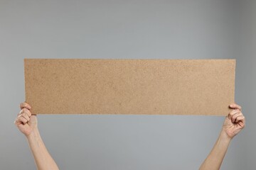 Woman holding blank cardboard banner on grey background, closeup. Space for text