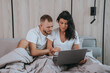 © Iona - Concentrated couple with laptop discussing something in bed, home interior