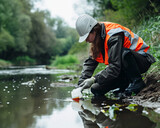 Fototapeta  - Environmental engineer in safety vest taking water sample from river. Eco-monitoring and conservation of natural water resources concept
