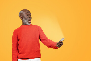 Wall Mural - Shocked elderly African American man in a red sweater and white pants stares at his smartphone