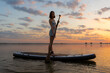 © Yekatseryna - athletic woman on SUP paddle boarding through shining water at sunset. aesthetically wide shot. Freedom happy female relaxing on surfboard on a lake