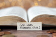 © Marinela - God loves a cheerful giver, handwritten text note in front of open holy bible book and golden coin money with bokeh background. Christian biblical concept of giving, tithing, and religious offering.
