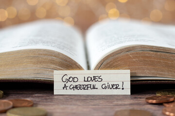 god loves a cheerful giver, handwritten text note in front of open holy bible book and golden coin m