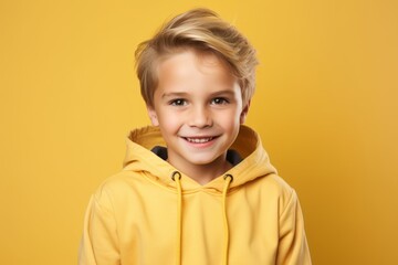 Portrait of a smiling little boy in a yellow hoodie on a yellow background