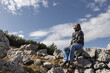 © Guzel - Adult gray-haired man sitting on a rocky fence against a cloudy sky and looking at the clouds, Austria