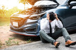© sorapop - Young businessman wearing white shirt and call roadside assistance. Worried mature man holding his head by hands sitting near his broken car with raised hood on the roadside of a rural road.
