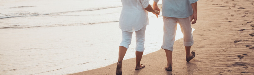 Couple of old mature people walking on the sand together and having fun on the sand of the beach enjoying and living the moment. Two cute seniors in love having fun..