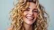 © buraratn - Blonde woman with curly beautiful hair smiling on gray background.