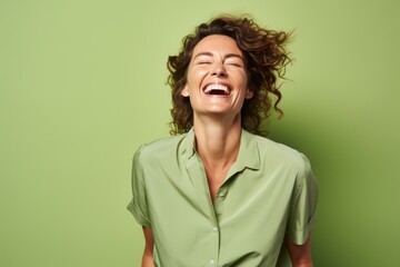 Wall Mural - Portrait of a happy young woman laughing with closed eyes against green background