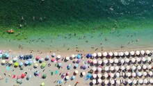 Drone Aerial View Of A Beach Filled With People On A Hot Summer Day. High Holiday Season. White Sun Umbrellas In A Row On A Perfect Sandy Beach. The Purest Transparent Adriatic Sea