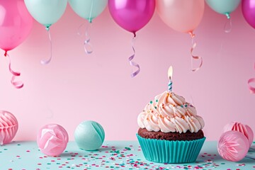 Cupcake with blue frosting and a lit candle, balloons and confetti in the background