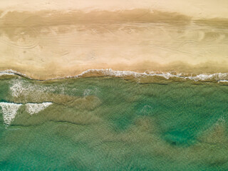 Wall Mural - The view from above is a mesmerizing seascape with waves, a sandy beach and turquoise water. A beautiful picture from a drone, from a bird's-eye view. Copy space, nature background, Mockup.