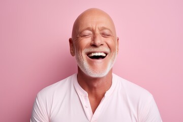 Wall Mural - Portrait of a happy senior man with white beard laughing against pink background