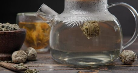 Wall Mural - Timelapse of Blooming flower tea ball brewing in a glass teapot with Hot boiling water on wooden background