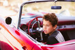 Young boy sitting in red classic car pretending driving