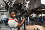 Fototapeta  - African male auto-mechanic repairing car brakes under the car in auto service