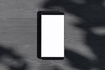 Poster - Close up of empty white smartphone on dark wooden surface with leaf shadows. Presentation concept. Mock up, 3D Rendering.