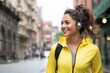 Sideways shot of pensive brunette young woman looks away into distance wears headphones in city outdoors returns home from workout leads active lifestyle.