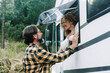 Happy adult couple enjoy travel  destination with motorhome camper van vanlife lifestyle. Woman at the window inside and man outside with green forest woods in background. Alternative life vacation