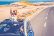 © simona - Happy women traveler enjoy road trip with a convertible car. One woman outside the roof have fun. Scenic desert destination. Car driving. Excited couple of friends in a vehicle on travel. Adventure