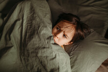 Scared boy hiding under blanket in bed at home