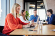 © Westend61 - Blond businesswoman working on laptop and sitting with colleagues in office