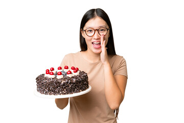 Young Asian woman holding birthday cake over isolated chroma key background shouting with mouth wide open