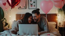 Happy loving couple shopping online while lying in bed and using laptop with heart shape balloons