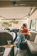 © simona - Handsome man with glasses sitting inside camper van, looking into the distance and smiling. Camping, outdoor activity, road trip, nature concept.