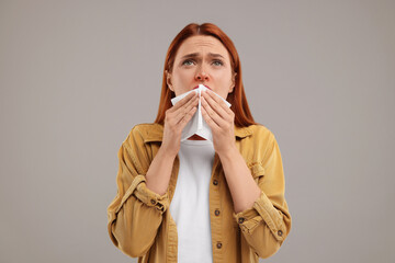 Poster - Suffering from allergy. Young woman with tissue sneezing on grey background