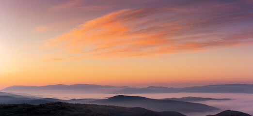 Wall Mural - panorama of a sky above the carpathian mountain range with fog in the valley at dawn. clouds in red 