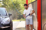 Fototapeta  - Happy man washing auto with high pressure water jet at outdoor car wash
