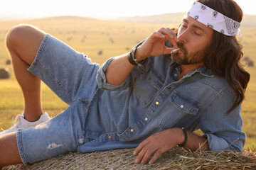 Canvas Print - Hippie man smoking joint on hay bale in field