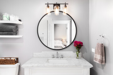 A bathroom detail with a white cabinet, black circular mirror, and light fixture, and a view to the bedroom.