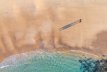 Aerial View Of A Couple Walking On A Wide Sandy Beach Castling Long Shadows