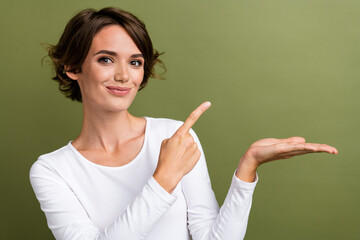 Poster - Photo portrait of pretty young girl point palm hold empty space wear trendy white outfit isolated on khaki color background