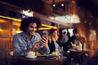 © Marko Geber - Smiling young man using smartphone in a cafe