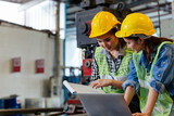 Fototapeta  - Two female engineers or technician worker wearing safety hard helmet discuss project in industry manufacturing factory. woman using laptop checking work, team colleague note on checklist document