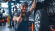 © Oulaphone - Smiling mechanic showing thumbs up with car tire in the car repair shop.