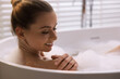 Beautiful woman taking bath in tub with foam indoors, closeup. Space for text