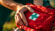 close-up of a hand holding a red first aid kit with a white cross on it