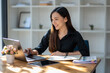 © Wasana - Freelance Asian woman working happily on laptop in the morning with sunlight shining through the glass on the table.