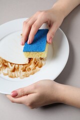 Sticker - Woman washing dirty plate with sponge on light grey background, closeup